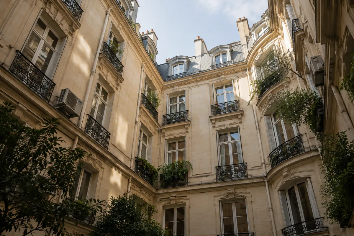 Cour intérieure d'un immeuble haussmannien vue d'en bas, façades en pierre de taille, balcons en fer forgé et quelques unités de climatisation (illustration générée par IA)